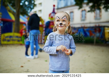Little preschooler girl with cat face painting, making funny grimace outdoors. Children face painting. Creative activities for kids Royalty-Free Stock Photo #2029131425