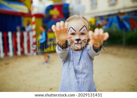 Little preschooler girl with cat face painting, making funny grimace outdoors. Children face painting. Creative activities for kids Royalty-Free Stock Photo #2029131431