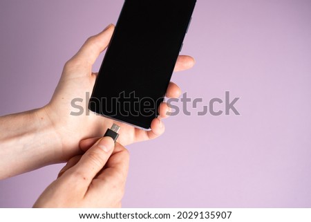 Mobile smart phones charging. Woman hands plugging a charger in a smartphone on purple background Royalty-Free Stock Photo #2029135907