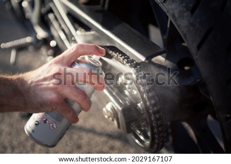 Man's hand using spray can to clean and protect motorbike chain. Concept of maintenance and lubrication of the motorcycle chain. Royalty-Free Stock Photo #2029167107