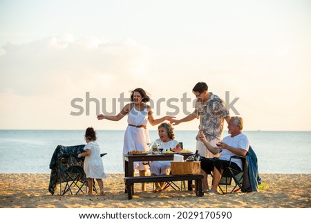 Happy Asian family on holiday vacation. Group of multi generation family little girl with parents and grandparents relax and enjoy with dinner party and dancing together on the beach at summer sunset. Royalty-Free Stock Photo #2029170590