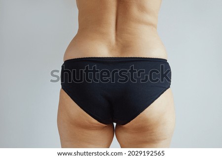 Rear view of a plump woman in black panties. Studio photo on gray background.