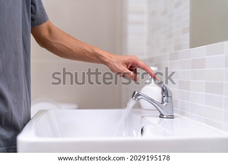 The faucet in the bathroom with running water. Man keeps turn off the water to save water energy and protect the environment. save water concept Royalty-Free Stock Photo #2029195178