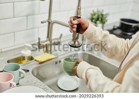 Close up of young African-American woman washing dishes at home while doing chores on weekend, copy space