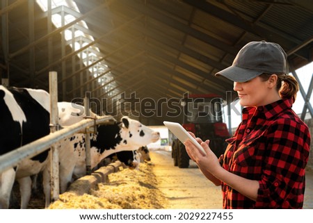 Farmer with tablet computer inspects cows at a dairy farm. Herd management concept. Royalty-Free Stock Photo #2029227455
