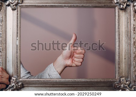 Thumbs up on gilded picture frame pink background