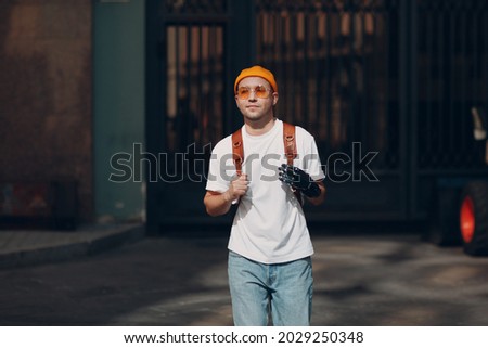 Young disabled man with artificial prosthetic hand in casual clothes and backpack walking at sunny city european street outdoor Royalty-Free Stock Photo #2029250348