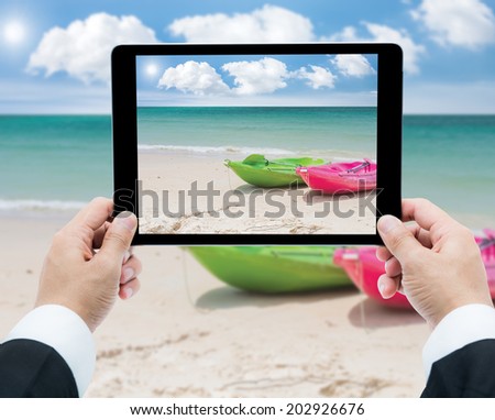 Businessman hands tablet taking pictures canoe on beach and sea
