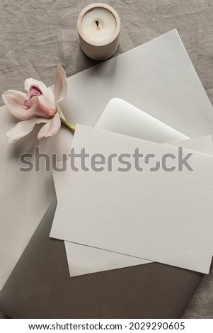 Blank paper sheet card with mockup copy space, laptop computer, pink flower, candle on neutral linen cloth background. Minimal aesthetic business brand, wedding invitation template. Flat lay, top view