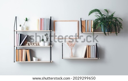 Shelves with books and decor hanging on light wall Royalty-Free Stock Photo #2029299650