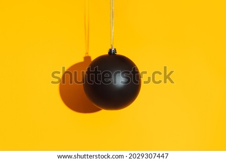 Black matte bauble with hard shadow on yellow background.