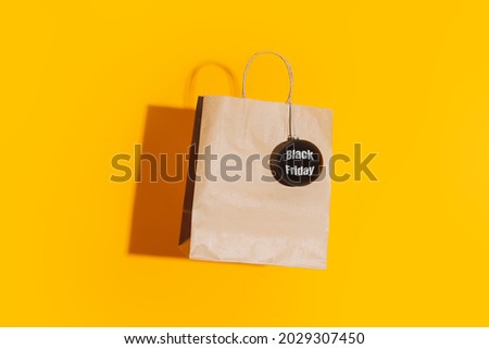 Paper bag with black matte bauble with black friday lettering against yellow background.