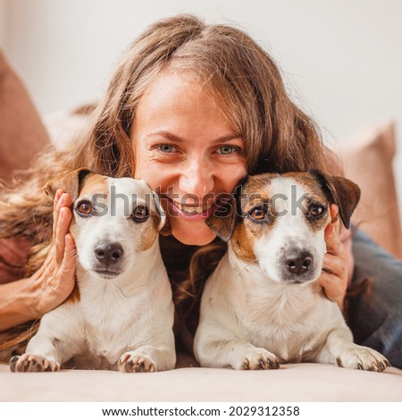 Happy girl hugging dogs. Female resting at home on brown couch. Smiling woman with pet on sofa