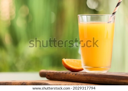 Board with glass of tasty orange juice on table outdoors