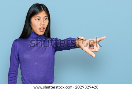 Beautiful young asian woman wearing casual clothes pointing with finger surprised ahead, open mouth amazed expression, something on the front 