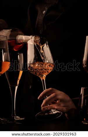 Sommelier pouring rose wine into glass at wine tasting in winery, bar or restaurant. Black toned image Royalty-Free Stock Photo #2029331963