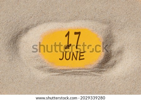 June 17. 17th day of the month, calendar date. Hole in sand. Yellow background is visible through hole. Summer month, day of the year concept.