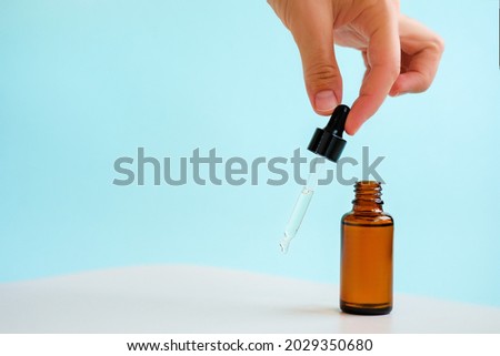 Female hand holds the essential oil falling from the amber glass dropper. Bottle of cosmetic oil with a pipette. Copy space. Light blue background. Royalty-Free Stock Photo #2029350680