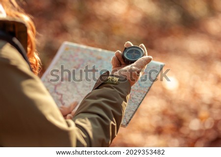 Active young woman holding a compass and reading a map while taking a hiking break, having fun and relaxing while spending autumn day outdoors Royalty-Free Stock Photo #2029353482
