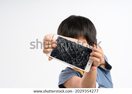 Asian boy about 4 years old holding mobile phone with broken screen glass on white background