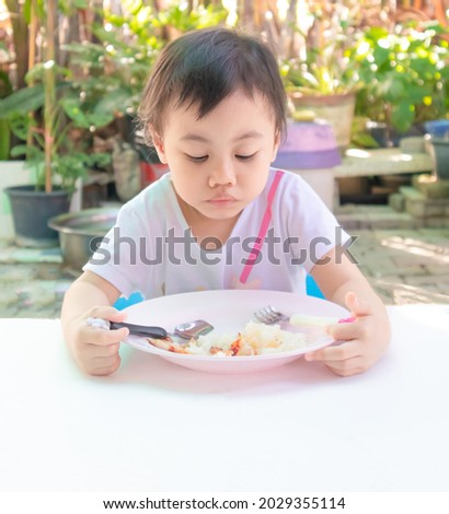 Unhappy 3 years old cute baby Asian girl, little toddler child eating disorders tasteless food for lunch, loss of appetite. Healthy eating habits for kids concept.