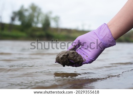 River soil composition concept. Woman a scientist takes a sludge sample from a river close up. Royalty-Free Stock Photo #2029355618