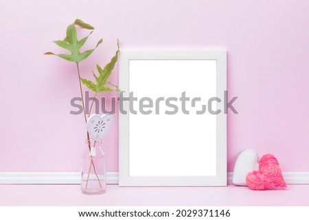 White vertical picture frame, heart-shaped ornaments and fern leaves in front of pink wall. Feminine poster mockup. Blank image area masked with clipping path.