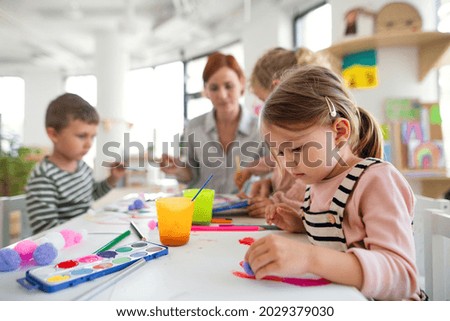 Group of small nursery school children with teacher indoors in classroom, painting. Royalty-Free Stock Photo #2029379030