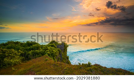 Breathtaking seascape. Spectacular view from Uluwatu cliff in Bali. Sunset time. Blue hour. Ocean with motion foam waves. Cloudy sky. Nature concept. Soft focus. Slow shutter speed.