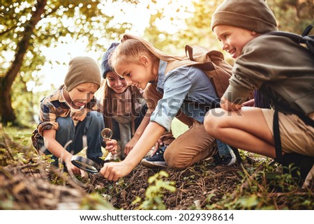 Happy children boys and girls in casual clothes with backpacks making bonfire with magnifying glass together in green forest during school camping activity on sunny day, smiling kids exploring nature Royalty-Free Stock Photo #2029398614