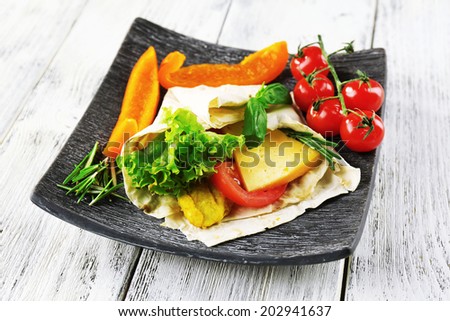 Veggie wrap filled with chicken and fresh vegetables on wooden table