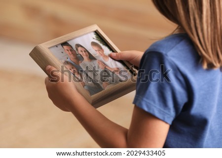 Little girl holding framed family photo on blurred background, closeup