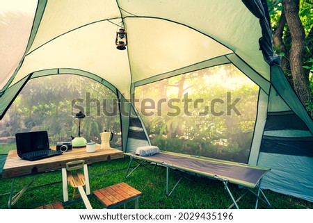 The folding bed inside the tent in the morning Oil lamps and coffee sets, notebooks on a wooden camping table, and outdoor ideas. Royalty-Free Stock Photo #2029435196