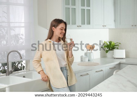 Woman drinking tap water from glass in kitchen Royalty-Free Stock Photo #2029443245