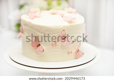 Birthday cake for a girl decorated with white cream with pink butterflies on the background of a home interior.
