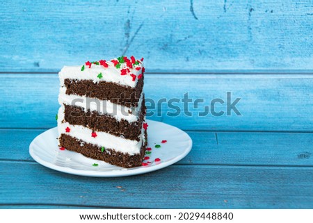 A piece of chocolate sponge cake with a layer of butter cream located on the left. Blue background. Red-green dusting.