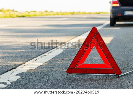 Red emergency stop sign (red triangle warning sign) and broken car on a road