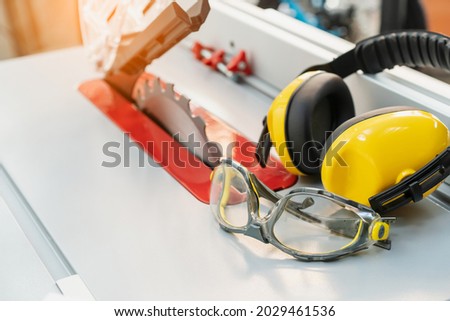Safety glasses and Earmuffs on Electric saw table in workshop .Work safety concept . selective focus   Royalty-Free Stock Photo #2029461536