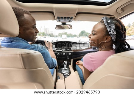 Back view of smiling young black lovers man and woman in casual comfortable outfit looking at each other, excited afro american couple having car trip by comfy luxury auto, shot from backseat Royalty-Free Stock Photo #2029465790