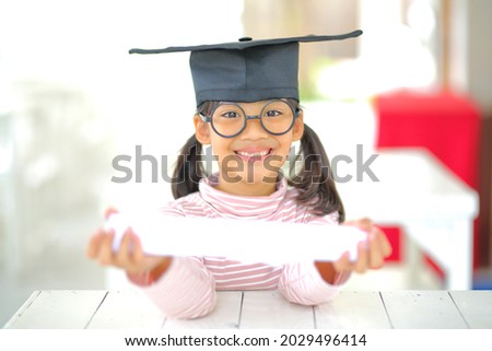 A little girl asia looks happy while celebrating his graduation and holding a diploma and graduation cap  which increases the development and enhances outside the classroom learning skills concept.