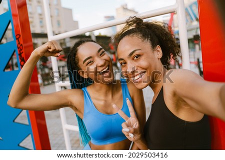 Two happy young fit african fitness women taking a selfie while standing at the sportsground