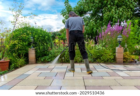 Cleaning stone slabs on patio with the high-pressure cleaner. Person worker in rubber boots cleaning the outdoors floor.