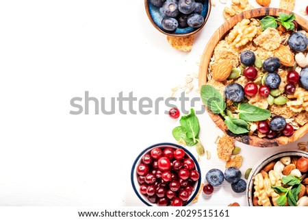 Sugarless muesli in bowl and ingredients for healthy breakfast. Granola, nuts, blueberry, cranberry, greek yoghurt, whole grain flakes on white table, top view