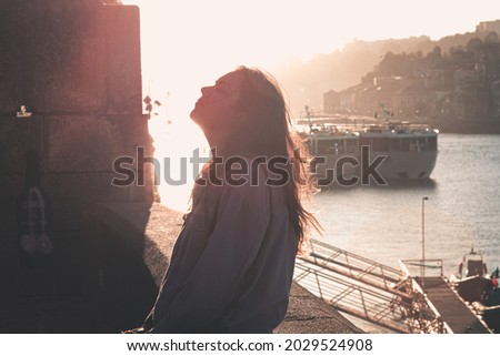 Woman closing his eyes and looking up while exhaling and relaxing in the docks of the city, during a colorful sunset, mental health concept, tourism