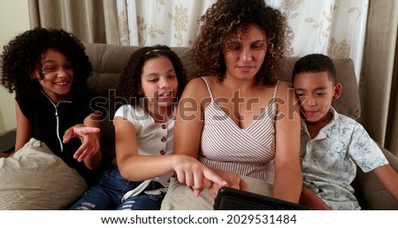 Brazilian mother and children staring at cellphone screen together at home sofa surprised reaction