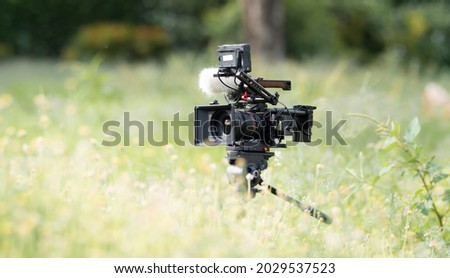 a movie camera or documentaries equipped with monitors for cinematographers. and a boom mic for recording good quality sound. Placed in the middle of a flower field on a beautiful sunny day
