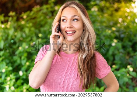 Young pretty woman at outdoors keeping a conversation with the mobile phone with someone