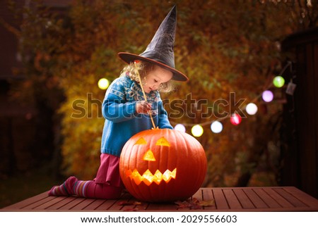 Kids trick or treat in Halloween costume. Children in colorful dress up with candy bucket on suburban street. Little girl trick or treating with pumpkin lantern. Autumn holiday fun.