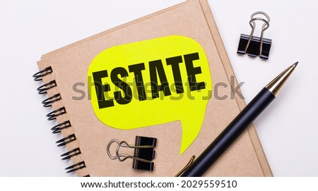 On a light background, a brown notebook, a black pen and paper clips, and a yellow card with the text ESTATE. Business concept.