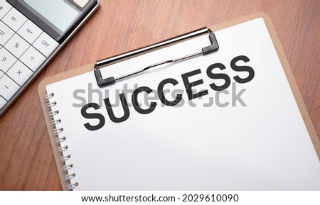 Notepad with text success on wooden background with clips, pen and calculator
